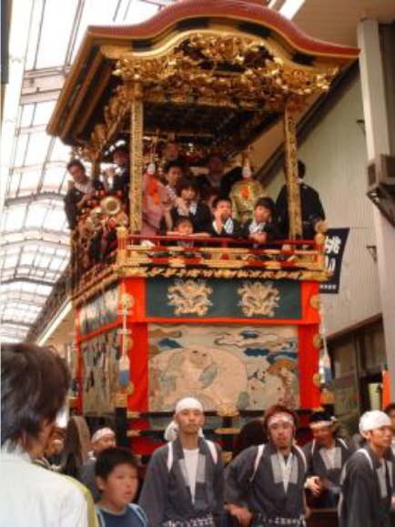 大津祭の曳山。金色の装飾と朱塗りの欄干の上に囃子方が乗り、下では法被姿の曳き手が曳山を囲んでいる。