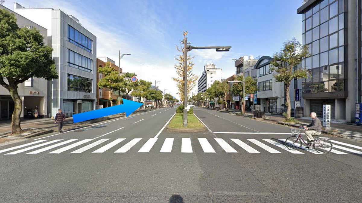 中央大通りと中町通の交差点。緑の中央分離帯と広い横断歩道、両側に街路樹とビルが並ぶ。